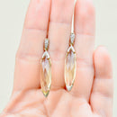 Gold earrings with clear gemstones held in a hand against a light background