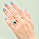 Hand wearing a green gemstone ring with floral nail design on a light background