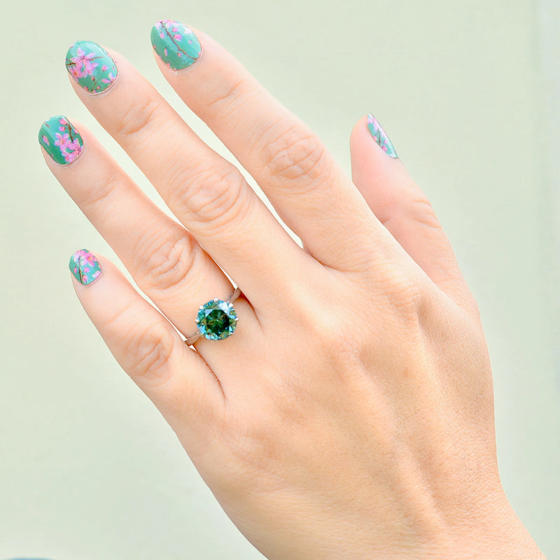 Hand wearing a green gemstone ring with floral nail design on a light background