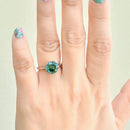 Hand wearing a ring with a green gemstone on a light background