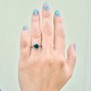 Hand wearing a ring with a green gemstone against a light background