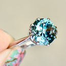 Close-up of a ring with a large blue gemstone held by a hand.