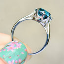 Silver ring with a blue gemstone held by a hand with floral nail polish on a beige background