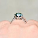 Silver ring with a green gemstone on a finger against a neutral background